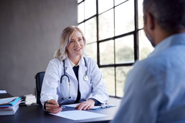 Kadın doktor bir hastayı dikkatle dinliyor ve tıbbi tedavi ve tedavi sağlıyor. Sağlık uzmanı özel bir kliniğe yaptığı ziyarette sağlık seçeneklerini açıklıyor. Detaylı bir konsültasyon sırasında bir hastayla konuşan kadın pratisyen.