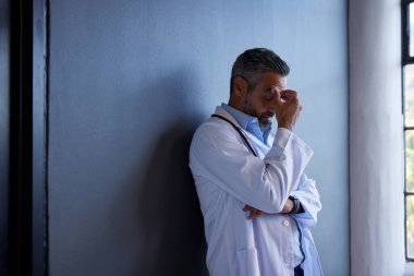 Hintli olgun doktor, özel klinikte fotokopi alanı olan bir duvara karşı stres ve yorgunluk belirtileri gösteriyor. Karışık ırk doktorları zorlu bir durumu sindirmeye çalışıyor. Stresli sağlık çalışanı portresi depresyon, tükenme ve ov