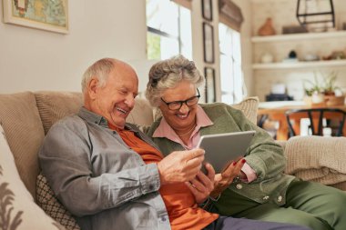 Evde dijital tablet kullanarak kanepede oturan son sınıf çifti. Yaşlı adam ve yaşlı kadın içeriği keşfediyor ve dijital tablette birlikte gülümsüyorlar. Kaygısız emekli çift sevinçle dokunmatik ekranı kullanırken bir anı paylaşıyorlar..