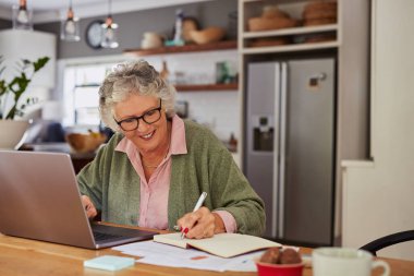 Yaşlı bir kadın dizüstü bilgisayar kullanırken belgeleri inceliyor ve evinde fotokopi odasıyla notlar alıyor. Ev ortamında dizüstü bilgisayar ve dizüstü bilgisayarla işleri yürüten güzel bir kadın. Kıdemli gülümseyen bayan gözlük takıyor ve bilgi topluyor. 