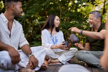 Bir grup yetişkin, huzurlu bir orman ortamında bir fincan çayı paylaşıyor. Bağlantının ve rahatlamanın keyfini çıkarıyorlar. Orta yaşlı bir adam holistik rehabilitasyon merkezinde gülümseyen melez bir kadın için çay dolduruyor. Karışık ırktan insanlar doğada rahatlar, eğlenirler.