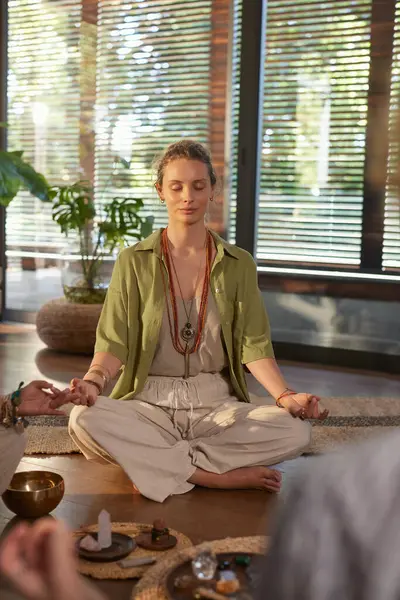 Huzurlu genç bir kadın grup terapisi sırasında meditasyon pozu veriyor. Sağlık merkezinde bilinçlilik ve nefes alma pratiği yapan bir kadın. Sakin bir kadın, gözleri kapalı, Mudra 'da el ele tutuşuyor. Etrafı kristaller ve sıcak güneş ışığıyla çevrili..