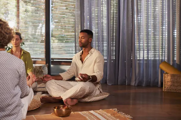 Genç siyahi adam huzur içinde dinlenme merkezinde meditasyon yapıyor. Gözleri kapalı çapraz oturan bir adam, farkındalık ve nefes alma egzersizleri yapıyor. Nilüfer pozisyonunda oturmuş, rahat bir şekilde meditasyon yapan yetişkin bir adam. 