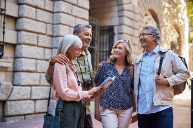Bir grup eski dost gezerken gülümsüyor ve bir rehber kitaba bakıyor. Son sınıf öğrencileri sokaklarda seyahat güzergahlarını planlarken mutlular. İki yetişkin çift kitap okuyup gülümserken yürüyüş turundan zevk alırlar..