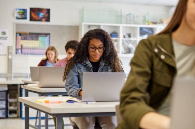 Kopya alanı olan bir sınıfta dizüstü bilgisayarla çalışırken gözlük takan çok ırklı ciddi bir kız öğrenci. Masasında çalışma materyalleriyle dizüstü bilgisayarda yazan Afrikalı Amerikalı bir kız. Erkekler ve kızlar bilgisayar dersi sırasında bilgisayar kullanıyor.