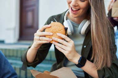 Dışarıda arkadaşlarıyla hamburger yiyen mutlu bir kız. Heyecanlıyken abur cubur yiyen güzel bir kız. Yemek molasının keyfini çıkarırken kablosuz kulaklık takan genç kız portresi.