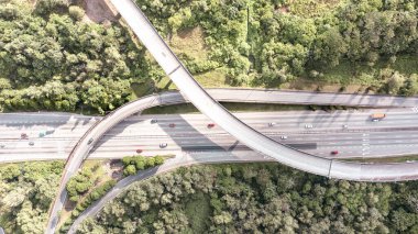 Altı şeritli bir otoyolun tam üstündeki hava manzarası. Asfalt yolunun üst manzarası tarladan ve ormandan geçiyor. Havadan. Otoyoldan geçen sedan arabalar. İHA 'nın üst görüntüsü. Hava fotoğrafı otoyolu.