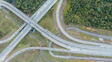 Güneşli bir günde şehrin havadan görünüşü ve üst geçidi. Malezya 'da yol trafiği. Şehir otoyolunun kavşaklarındaki hava manzarası. Araçlar yollarda gider. Sokakta giden araçların üst görüntüsü