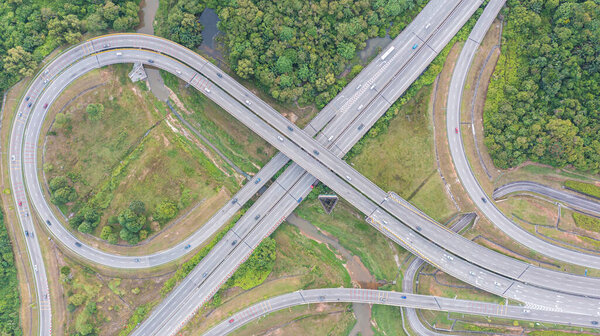 Aerial view of highway and overpass in city on a sunny day. Road traffic in city at Malaysia. Aerial view at junctions of city highway. Vehicles drive on roads. Top view of vehicles driving on street
