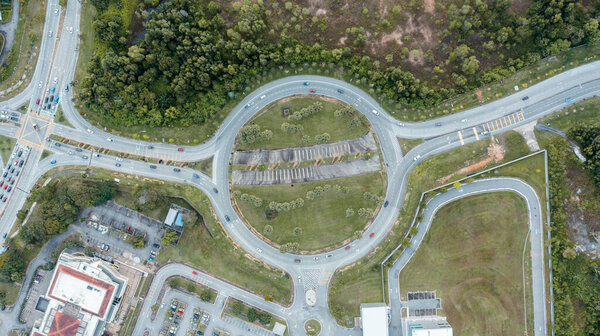 Top down aerial view of a traffic roundabout on a main road in an urban area of Malaysia. Aerial view of roundabout on a sunny day. Bird's eye view of a traffic roundabout, roads, lanes with cars
