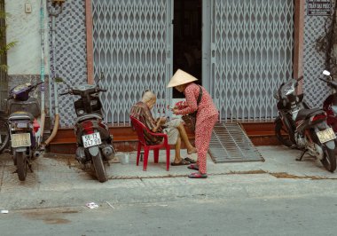 Ho Chi Minh City, Vietnam - 8 Kasım 2022: Geleneksel Vietnam elbisesi ve Non la başlıklı yaşlı kadın Saigon 'da yaşlı bir adama piyango bileti satıyor. Vietnam Yaşam Tarzı