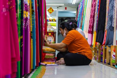 Ho Chi Minh City, Vietnam - 8 Kasım 2022: Kadın Vietnamlı kumaş satıcısı tekstil dükkanında envanter çıkarıyor. Yerde oturan ve stokları kontrol eden bir kadın. Saigon 'daki kumaş satıcısı