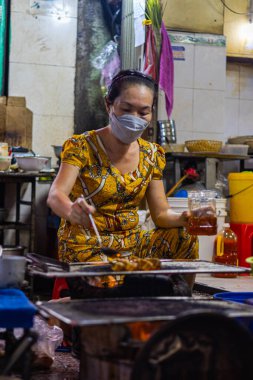 Ho Chi Minh Şehri, Vietnam- 9 Kasım 2022 Saigon sokaklarındaki sokak yemekleri dükkanı. Kadın aşçı ya da açık ateşte pişirme, yerel deniz ürünleri yemekleri. Yaşlı kadın yemek hazırlıyor.