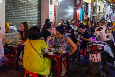 Ho Chi Minh Şehri, Vietnam- 9 Kasım 2022 Saigon sokaklarındaki sokak yemekleri dükkanı. Çok küçük masa ve sandalyelerde oturan müşteriler yerel deniz ürünleri yemeklerini severler. 1. Mıntıka 'da turistik ilgi