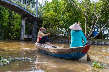 Ho Chi Minh City, Vietnam- 9 Kasım 2022: 2 Vietnamlı kadın, geleneksel konik şapkalı, Mekong nehrinde bir sandalda veya kanoda. Mekong Deltası 'nda tekne gezisi turistik bir eğlencedir.