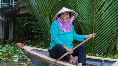 Ho Chi Minh Şehri, Vietnam- 9 Kasım 2022 Mekong deltasındaki sel basmış çivit bitkisi ormanında turizm kayığı. Mekong Delta kürekli tekneleri. Vietnamlı kadın, koni şeklinde bir güneş şapkası, gülüyor.