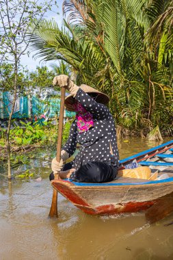 Ho Chi Minh Şehri, Vietnam- 9 Kasım 2022: Konik Vietnamlı şapkalı kadın kanoyu kontrol ediyor. Mekong deltasındaki turizm teknesi. Teknelerle turlar, Mekong Nehri 'nde turistik eğlence.