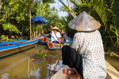 Ho Chi Minh Şehri, Vietnam- 9 Kasım 2022: Konik Vietnamlı şapkalı kadın kanoyu kontrol ediyor. Mekong deltasındaki turizm teknesi. Teknelerle turlar, Mekong Nehri 'nde turistik eğlence.