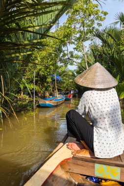 Ho Chi Minh Şehri, Vietnam- 9 Kasım 2022: Konik Vietnamlı şapkalı kadın kanoyu kontrol ediyor. Mekong deltasındaki turizm teknesi. Teknelerle turlar, Mekong Nehri 'nde turistik eğlence.