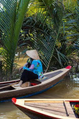Ho Chi Minh Şehri, Vietnam- 9 Kasım 2022: Konik Vietnamlı şapkalı kadın kanoyu kontrol ediyor. Mekong deltasındaki turizm teknesi. Teknelerle turlar, Mekong Nehri 'nde turistik eğlence.