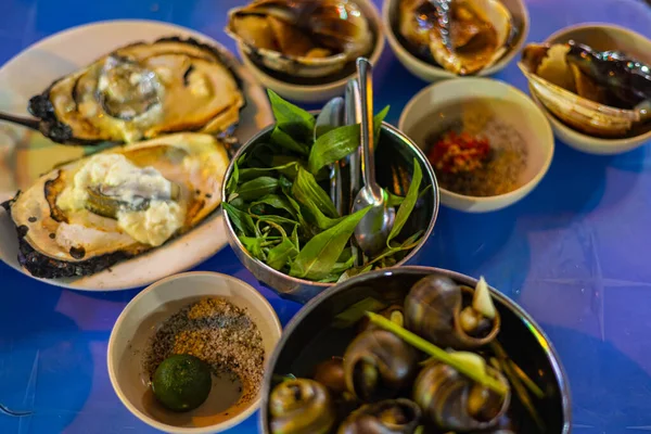 stock image Street food dishes in the streets of Saigon. Mussels, snails and oysters prepared in local Vietnamese style. Vietnam cuisine at night on the sidewalk