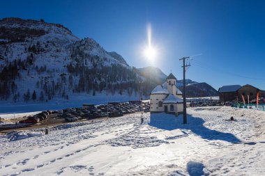 Falcade, İtalya - 14 Şubat 2023: Falcade dağ köyündeki kilise, vadideki kilise, karlı çatıları olan kış manzarası. Dolomitlerin yüksek dağları arasında gömülü.