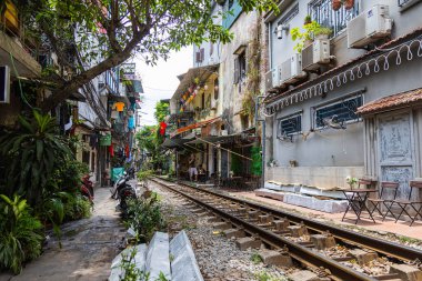 Hanoi, Vietnam - 28 Mayıs 2023 Hanoi 'deki tren yolu dar ve hareketli bir şerit. Bitkilerle süslenmiş birbirine yakın evler, geçen trenlerden birkaç santim uzaklıktadır. barlar ve kafeler rayları çiziyor