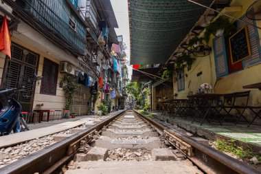 Hanoi, Vietnam - 28 Mayıs 2023 Hanoi 'deki tren yolu dar ve hareketli bir şerit. Bitkilerle süslenmiş birbirine yakın evler, geçen trenlerden birkaç santim uzaklıktadır. barlar ve kafeler rayları çiziyor