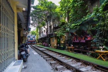 Hanoi, Vietnam - 28 Mayıs 2023 Hanoi 'deki tren yolu dar ve hareketli bir şerit. Bitkilerle süslenmiş birbirine yakın evler, geçen trenlerden birkaç santim uzaklıktadır. barlar ve kafeler rayları çiziyor