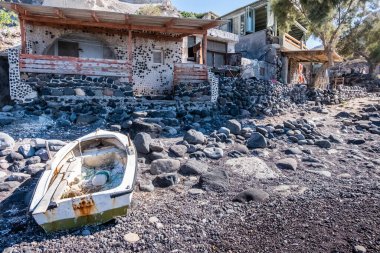 Santorini adasında eski paslı bir tekne. Taş ve ahşap bir sahil evinin önünde.