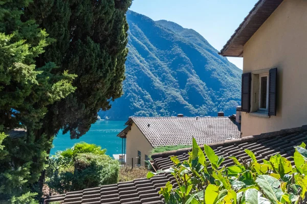 Lugano lake and the mountains seen from the top of a hill with the roofs of the houses in the foreground