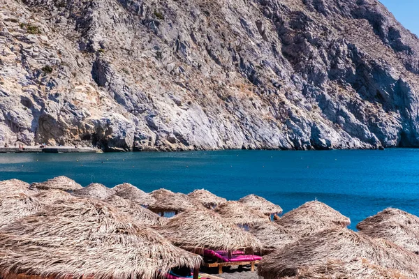 stock image Beach on the Greek island of Santorini with sunbeds and umbrellas. Beach is covered with fine black sand, and drops off sharply into the water.