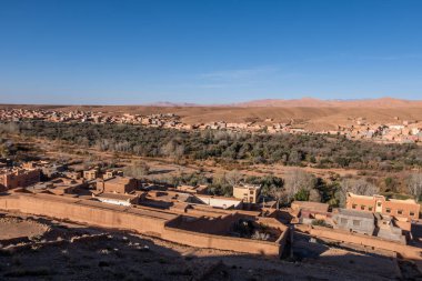 A traditional Berber village nestled in the foothills of the Atlas Mountains, with mud brick homes and palm groves dotting the landscape.