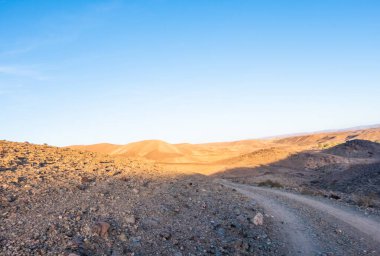 Crossing rocky mountains of the Morocco deseert. Black and red view with blue sky background near sunset time