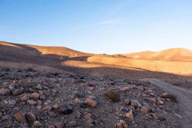 Crossing rocky mountains of the Morocco deseert. Black and red view with blue sky background near sunset time