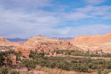 An old town on top of a hill in the middle of the desert in Morocco near an oasis of dates palm trees