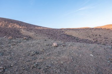 Crossing rocky mountains of the Morocco deseert. Black and red view with blue sky background near sunset time