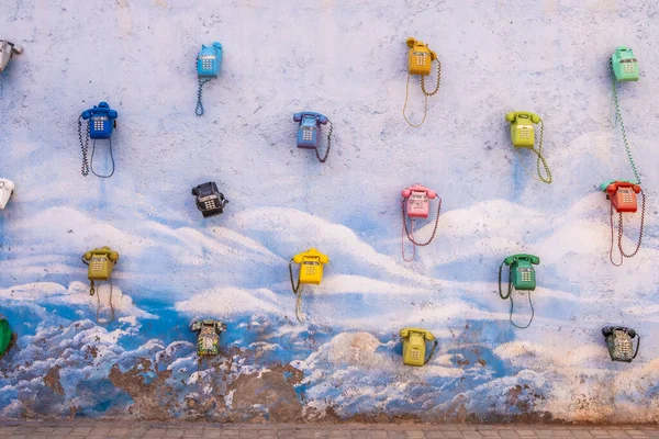 Colored telephones hanging in a blue and white wall. Urban art in the middle of nowhere