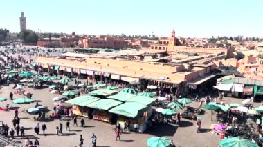 Jemaa el-Fnaa square on a sunny day full of people and green market stalls