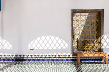 Windows with a yellow grate in a white wall with wooden bench and typical Moroccan ceramic on the floor. Marrakesh