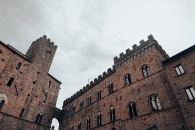 Medieval palace with turret in the central square of San Gimignano with gray cloudy sky in Tuscany, Italy