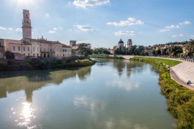 Calm waters of the Adige river which crosses Verona with gardens and a church with a bell tower in the background. Sunny day. Italy