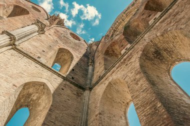 Low angle view of immense stone walls of an abandoned roofless medieval abbey near Siena in Tuscany, Italy