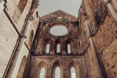 Low angle view of immense stone walls of an abandoned roofless medieval abbey near Siena in Tuscany, Italy