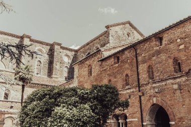 External view of the abbey of san galgano in tuscany. Green trees in leaf with the medieval building in the background