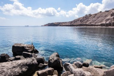 Santorini adasındaki sakin mavi Yunan denizi kumsaldaki siyah volkanik kayaların arkasından görüldü.