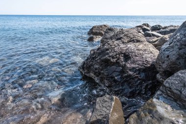 Kristal berrak deniz, Yunanistan 'daki Santorini adasının kara kayalarını okşar.