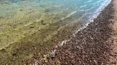Crystal Waters Grace Serene Shoreline. Yüksek kalite 4K görüntü. Kristal berraklığında suların sakin kıyı şeridini nazikçe öperken doğanın saf güzelliğinin tadını çıkarın. Bu dingin görüntü,