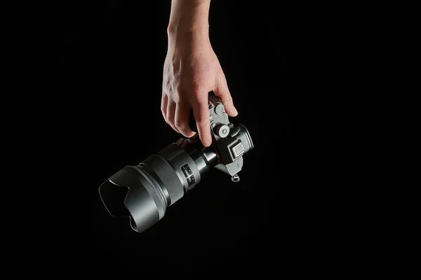 Genç fotoğrafçı elinde aynasız bir kamera tutuyor. Siyah arka planda izole edilmiş.