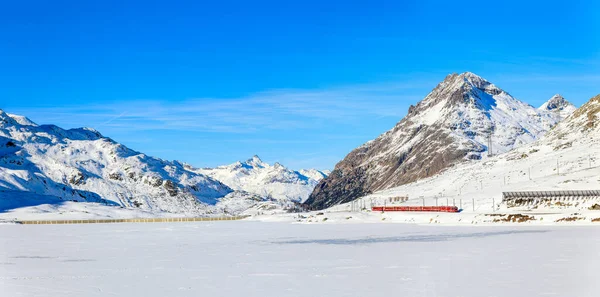 Panorama of the Lake Bianco with the red Rhaetian Rail passing along the lake side  and the Alps summit Piz Lagalb at the background